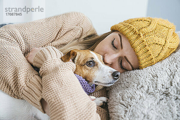 Frau in warmer Kleidung kuschelt mit Hund im Bett