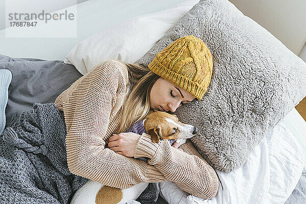 Frau in warmer Kleidung kuschelt mit Hund im Bett