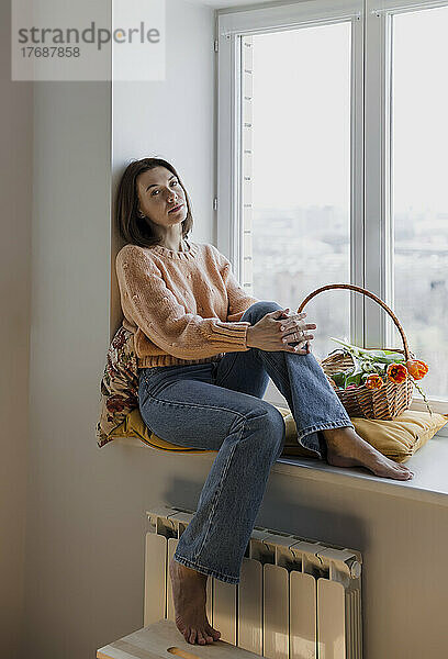 Reife Frau sitzt zu Hause auf der Fensterbank mit einem Korb voller Tulpen