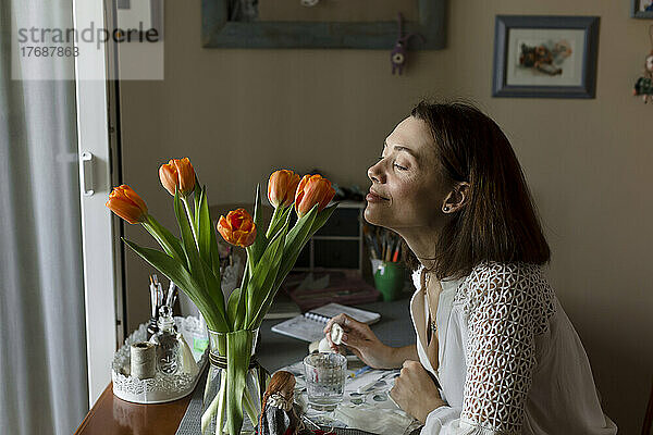 Reife Frau riecht Tulpenblüten auf dem heimischen Tisch