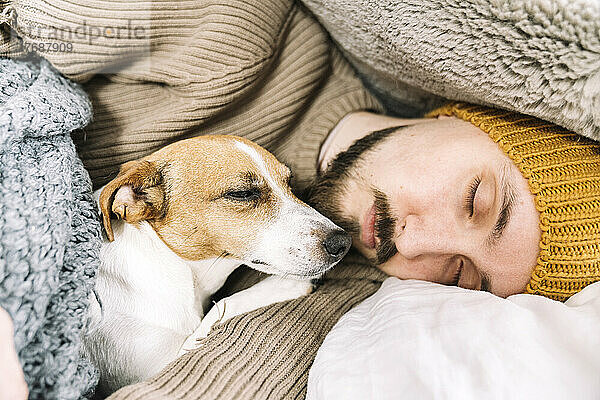 Erschöpfter Mann schläft voll bekleidet mit Hund im Bett