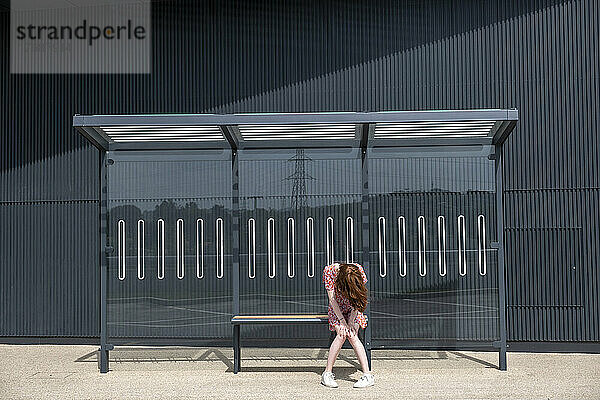 Traurige junge Frau sitzt allein an der Bushaltestelle