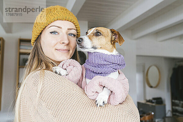 Frau trägt Wollmütze zu Hause und trägt Hund mit Schal