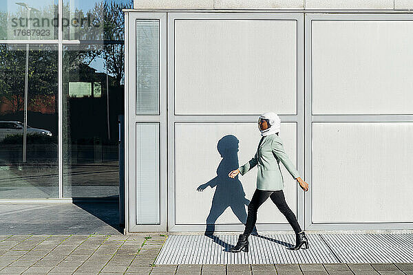 Junge Geschäftsfrau mit Weltraumhelm läuft am Bürogebäude vorbei