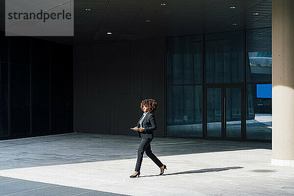 Geschäftsfrau hält Tablet-PC in der Hand und läuft vor Bürogebäude