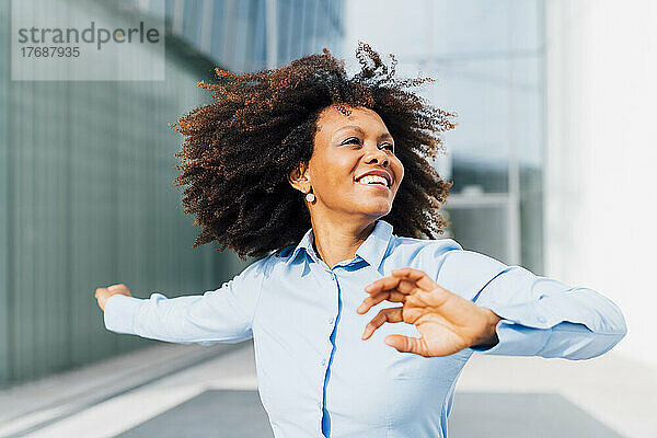 Lächelnde Afro-Geschäftsfrau tanzt an einem sonnigen Tag