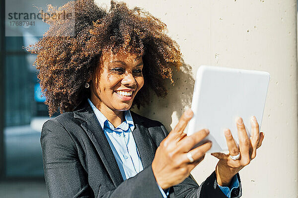 Glückliche Geschäftsfrau schaut auf den Tablet-PC  der sich auf eine Säule stützt