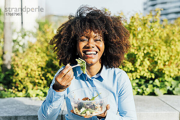 Glückliche Geschäftsfrau  die an einem sonnigen Tag Salat isst