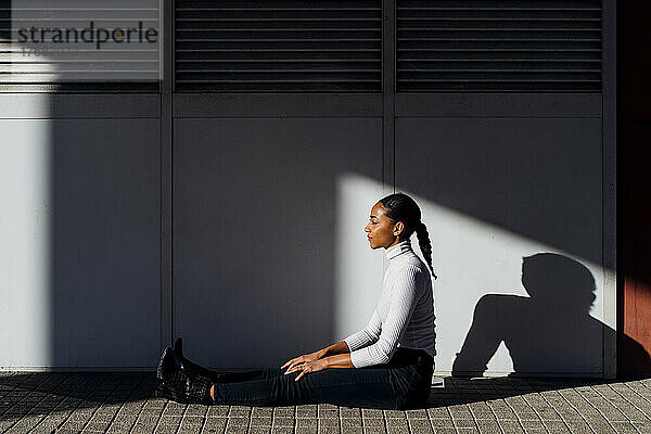 Junge Geschäftsfrau sitzt an der Wand auf dem Fußweg