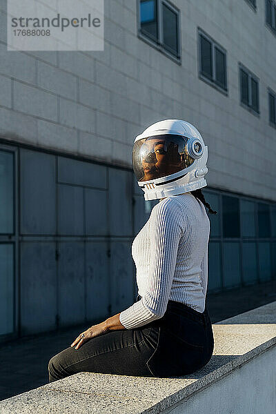 Junge Geschäftsfrau mit Weltraumhelm sitzt an der Wand