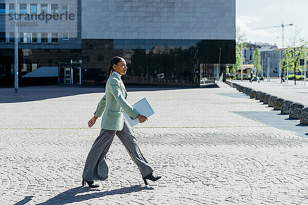Selbstbewusste Geschäftsfrau mit Laptop geht am Bürogebäude vorbei