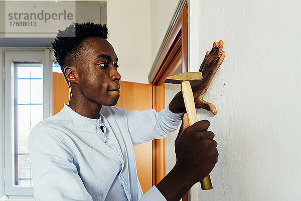 Junger Mann benutzt Hammer an Wand zu Hause