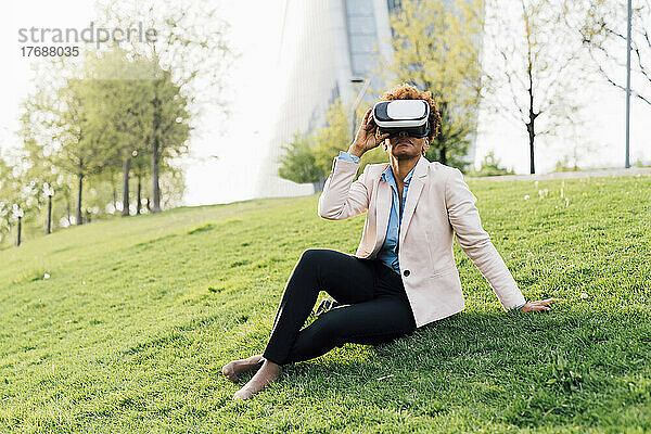 Geschäftsfrau mit Virtual-Reality-Simulator sitzt auf Gras