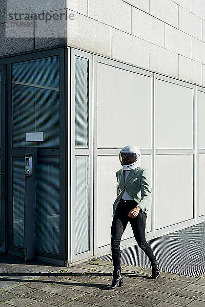 Geschäftsfrau mit Weltraumhelm läuft am Bürogebäude vorbei