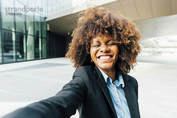 Glückliche Geschäftsfrau mit geschlossenen Augen macht ein Selfie vor dem Bürogebäude