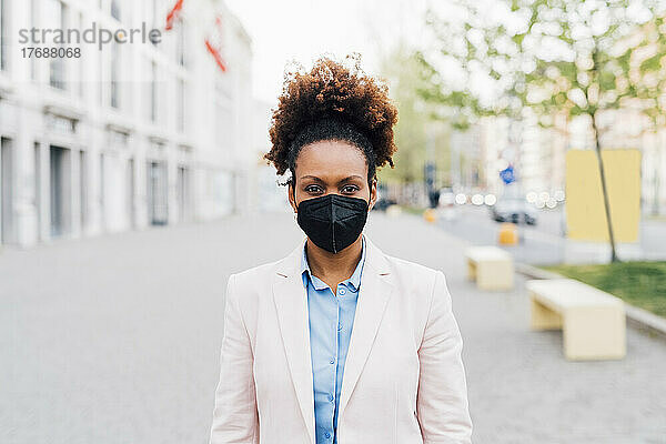 Afro-Geschäftsfrau trägt schützende Gesichtsmaske gegen Smog und steht auf dem Fußweg