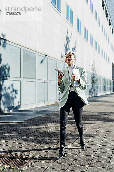 Junge Geschäftsfrau mit Smartphone läuft auf Fußweg am Bürogebäude vorbei