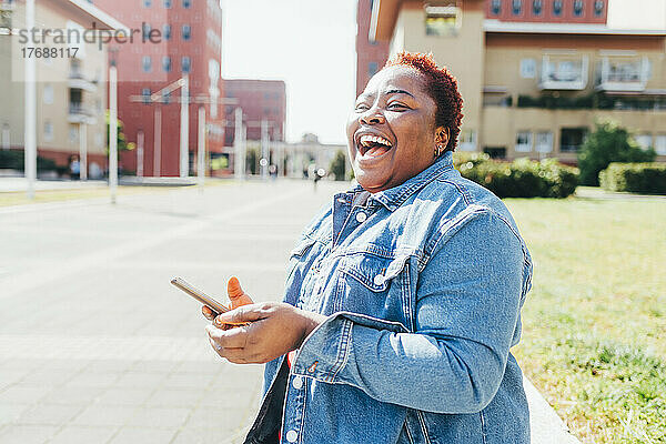 Glückliche Frau mit Smartphone lachend auf der Straße