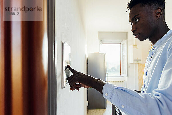 Junger Mann nutzt digitales Tablet an der Wand im Smart Home