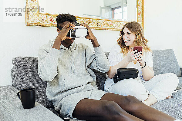 Mann mit Virtual-Reality-Simulator sitzt neben seiner Freundin zu Hause auf dem Sofa