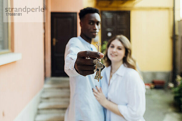 Junger Mann mit Freundin zeigt Schlüssel vor dem Haus