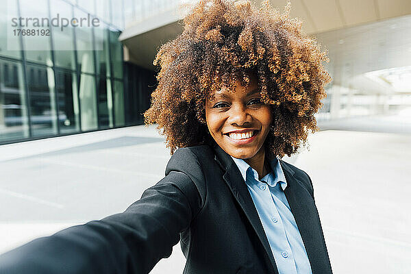 Lächelnde Afro-Geschäftsfrau  die vor dem Bürogebäude ein Selfie macht
