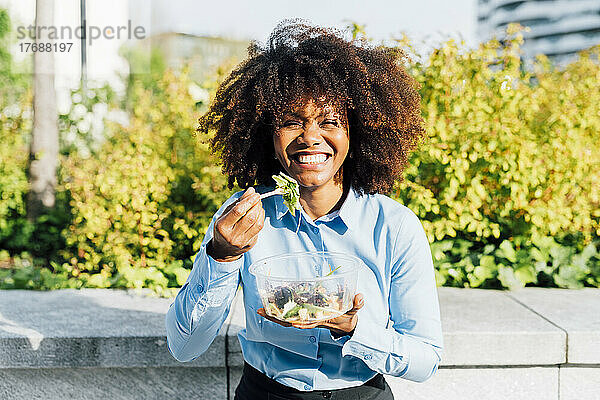 Glückliche Afro-Geschäftsfrau  die an einem sonnigen Tag Salat isst