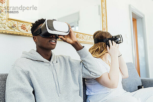 Junges Paar trägt Virtual-Reality-Simulatoren und sitzt zu Hause auf dem Sofa