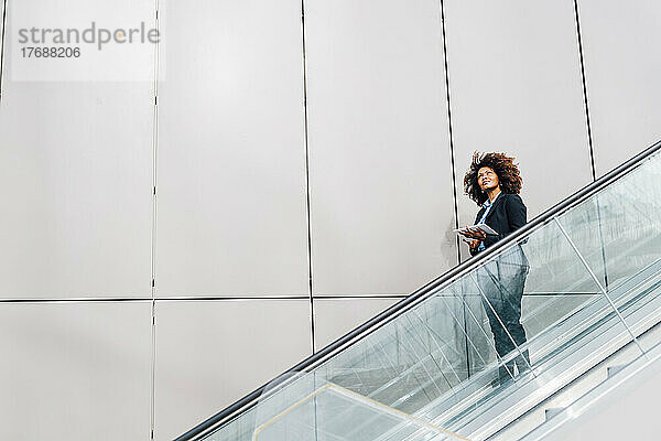 Afro-Geschäftsfrau hält Tablet-PC in der Hand und bewegt sich auf Rolltreppe nach unten