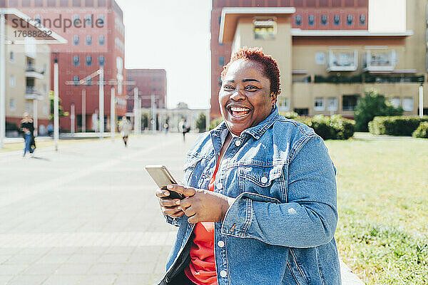 Glückliche Frau hält ihr Mobiltelefon in der Hand und genießt es an einem sonnigen Tag