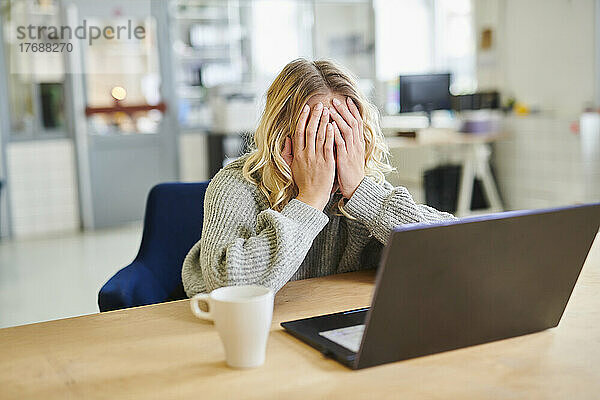 Verzweifelte junge Frau sitzt mit Laptop am Schreibtisch im Büro