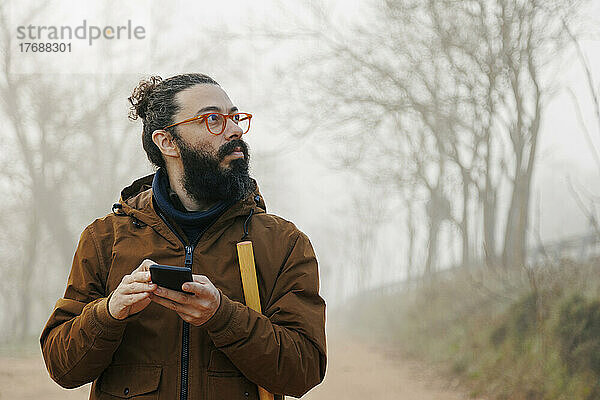 Reifer Mann mit Brille und Smartphone im Wald verloren