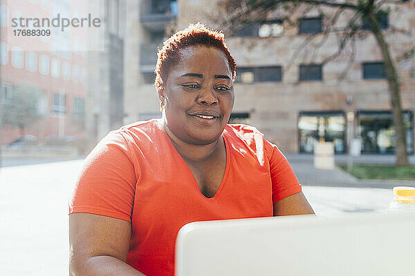 Lächelnde Frau  die an einem sonnigen Tag einen Laptop benutzt