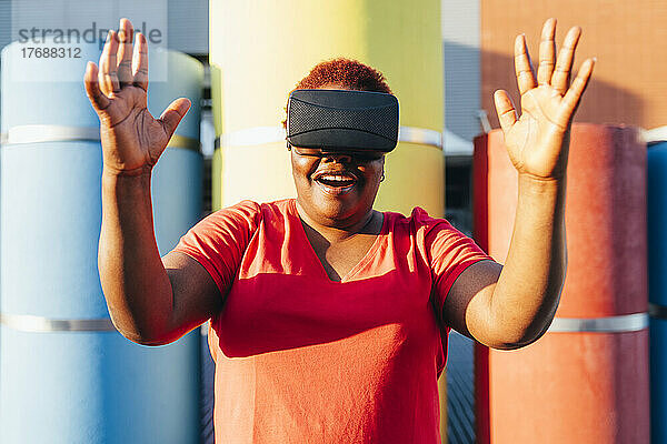 Glückliche Frau mit Virtual-Reality-Simulator gestikuliert an einem sonnigen Tag