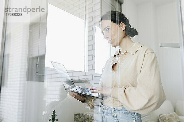 Junge Frau mit Laptop schaut durchs Fenster