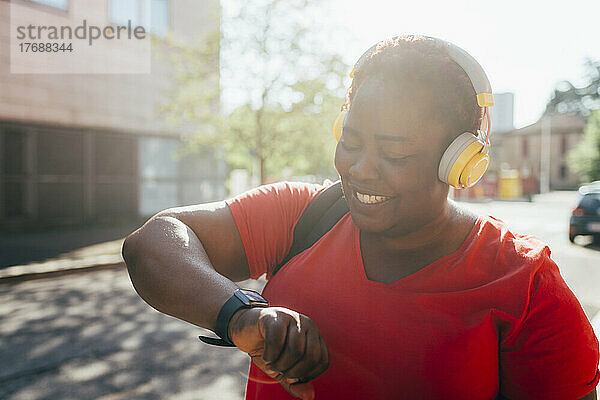 Glückliche Frau  die Musik hört und die Zeit auf einer Smartwatch überprüft