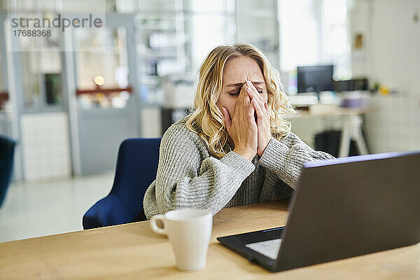 Frustrierte junge Frau sitzt mit Laptop am Schreibtisch im Büro
