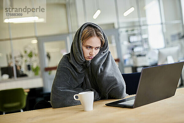 Frustrierte junge Frau in gemütlicher Loungewear sitzt mit Laptop am Schreibtisch im Büro