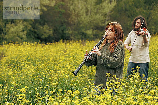 Frau übt Klarinette  während Mann Geige spielt und im Blumenfeld spaziert