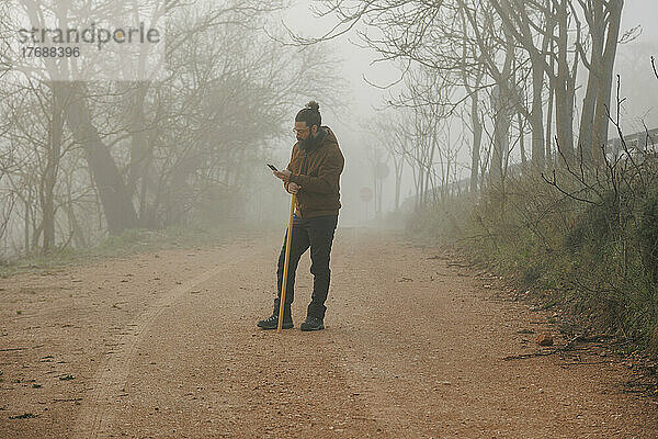 Reifer Mann benutzt Smartphone und steht auf Fußweg im Wald