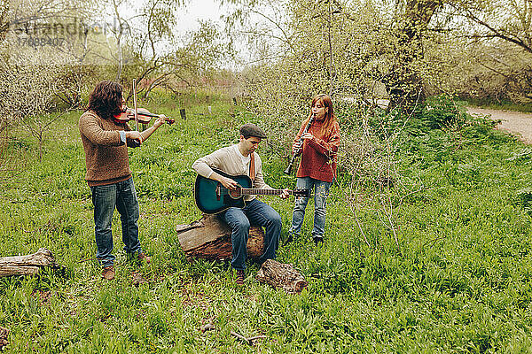 Mann übt Gitarre mit Freunden  die auf dem Feld Geige und Klarinette spielen