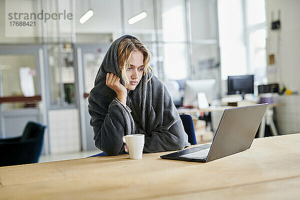 Junge Frau in gemütlicher Loungewear sitzt mit Laptop am Schreibtisch im Büro