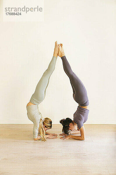 Freunde üben Handstand-Pose an der Wand im Yoga-Studio