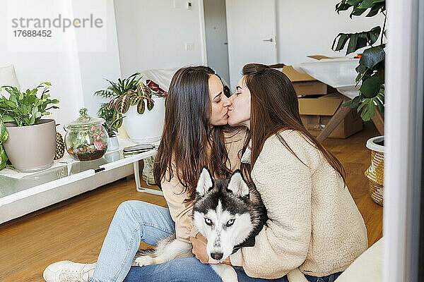 Lesbian couple kissing each other sitting with dog in apartment