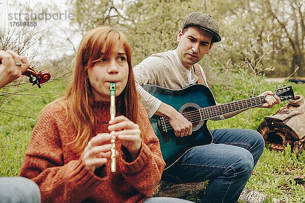 Mann mit Gitarre schaut Frau an  die auf dem Feld Tin Whistle spielt