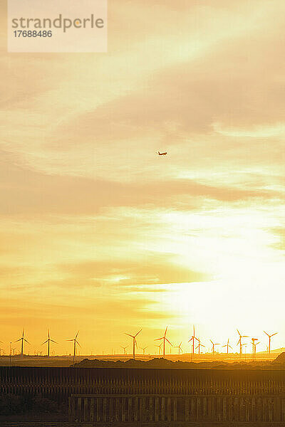 Flugzeug fliegt bei Sonnenuntergang über Windkraftanlage