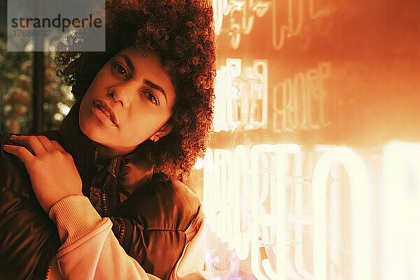 Junge schöne Frau mit Afro-Frisur lehnt an beleuchteter Wand