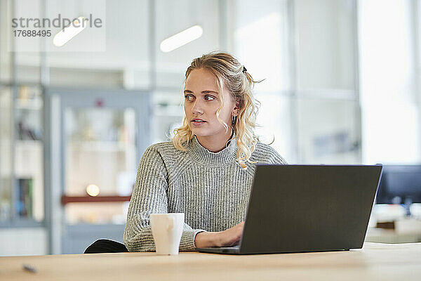 Junge Frau sitzt mit Laptop am Schreibtisch im Büro