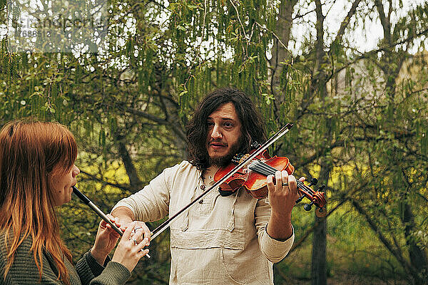 Mann übt Geige und schaut Frau beim Tin Whistle-Spielen an