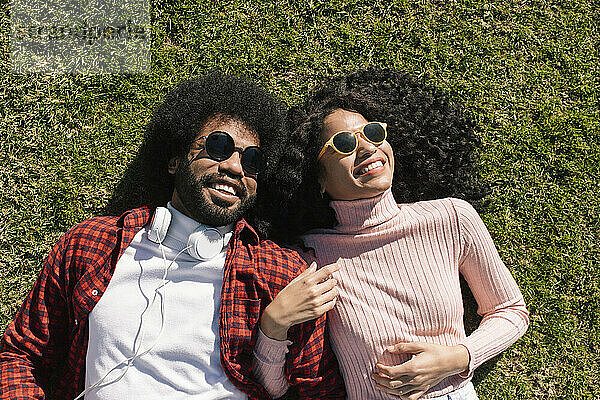 Glückliches Paar mit Sonnenbrille  das auf Gras liegt